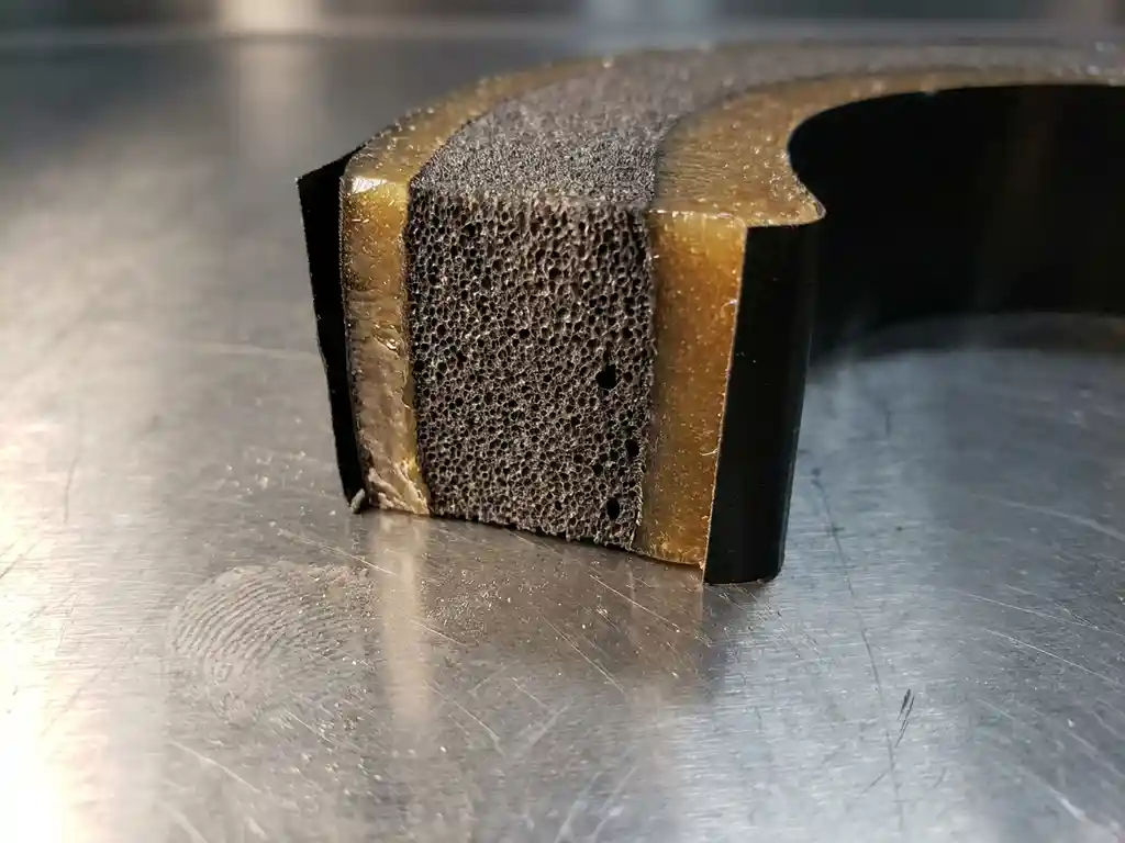 Querschnitt eines Industrie-Acrylschaumklebebands mit sichtbarem Schaumkern und Klebeschichten auf polierter Stahloberfläche.
